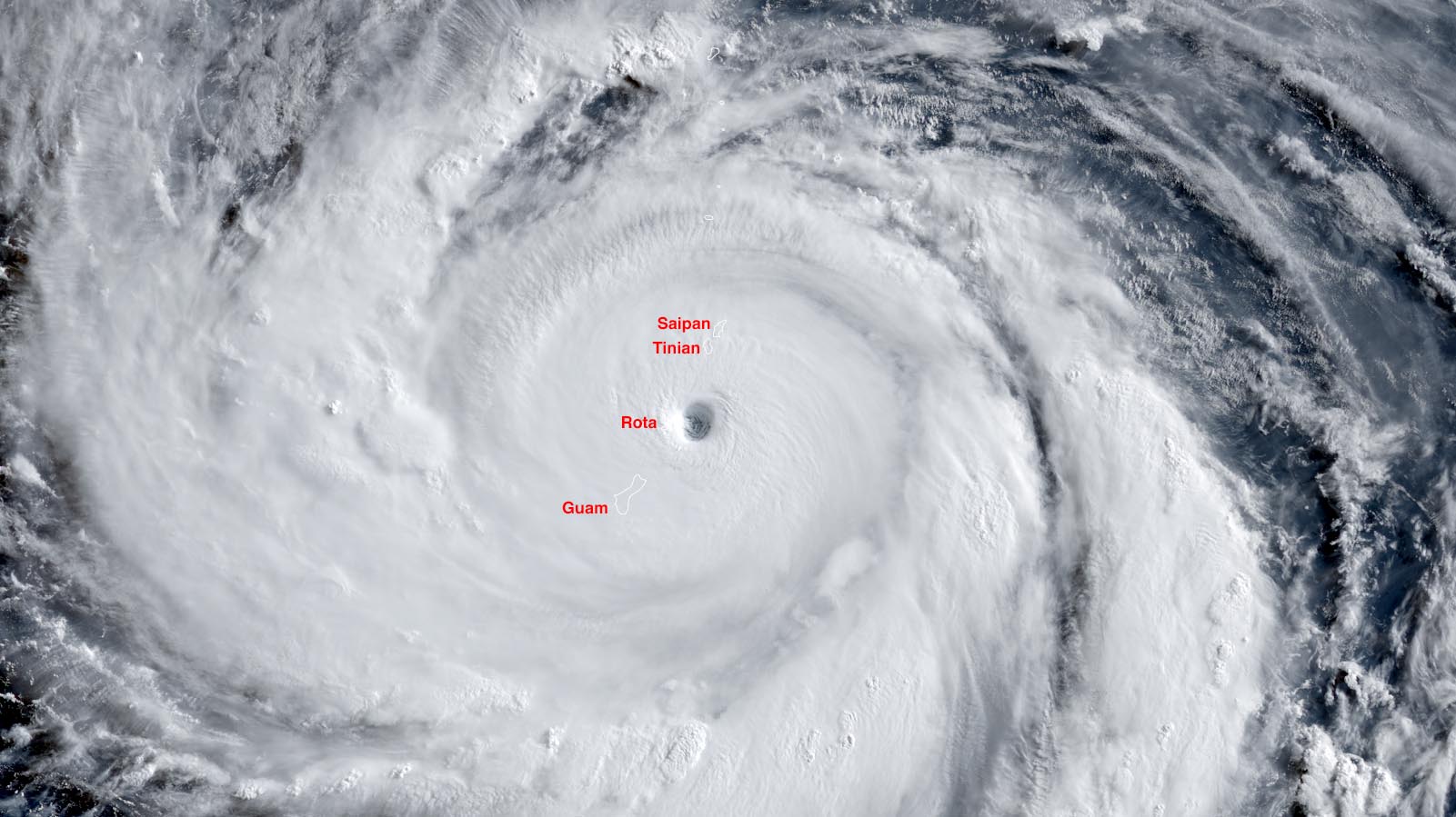 Visible-light satellite view of Super Typhoon Bavi at landfall, its bright cloud canopy filling the frame with a small dark eye centered over the island of Rota; Guam, Tinian and Saipan are labelled nearby, all inside the storm.